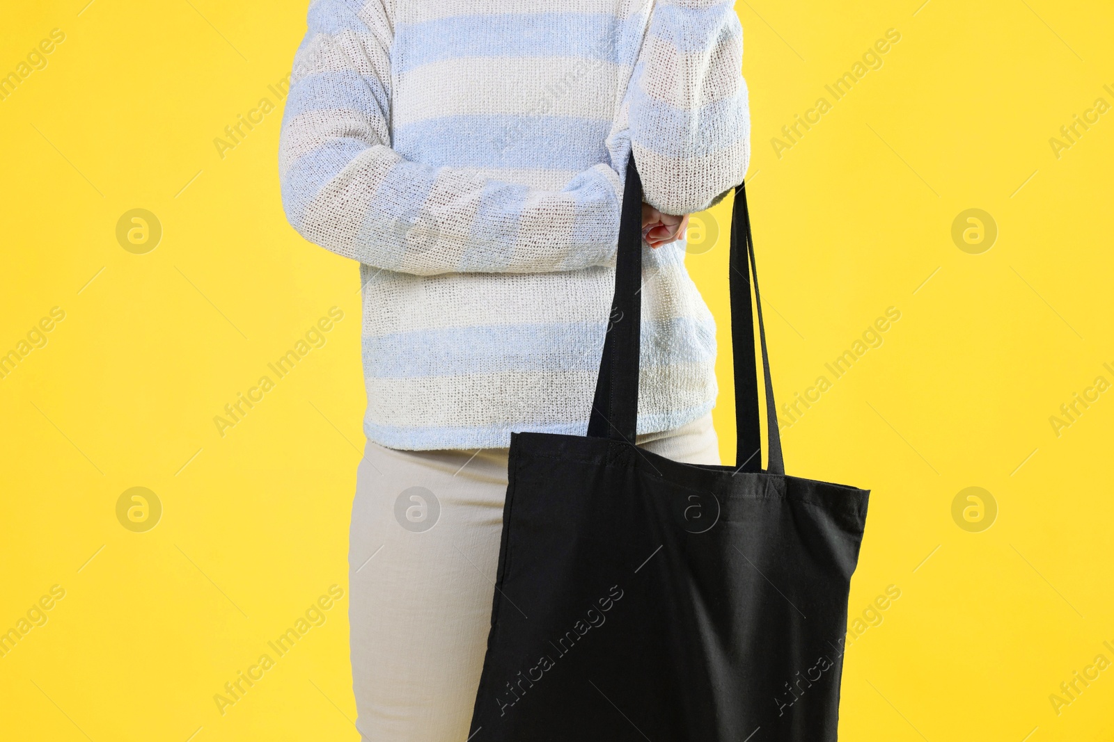 Photo of Woman with blank black shopper bag on yellow background, closeup. Mockup for design