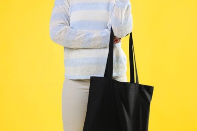 Woman with blank black shopper bag on yellow background, closeup. Mockup for design