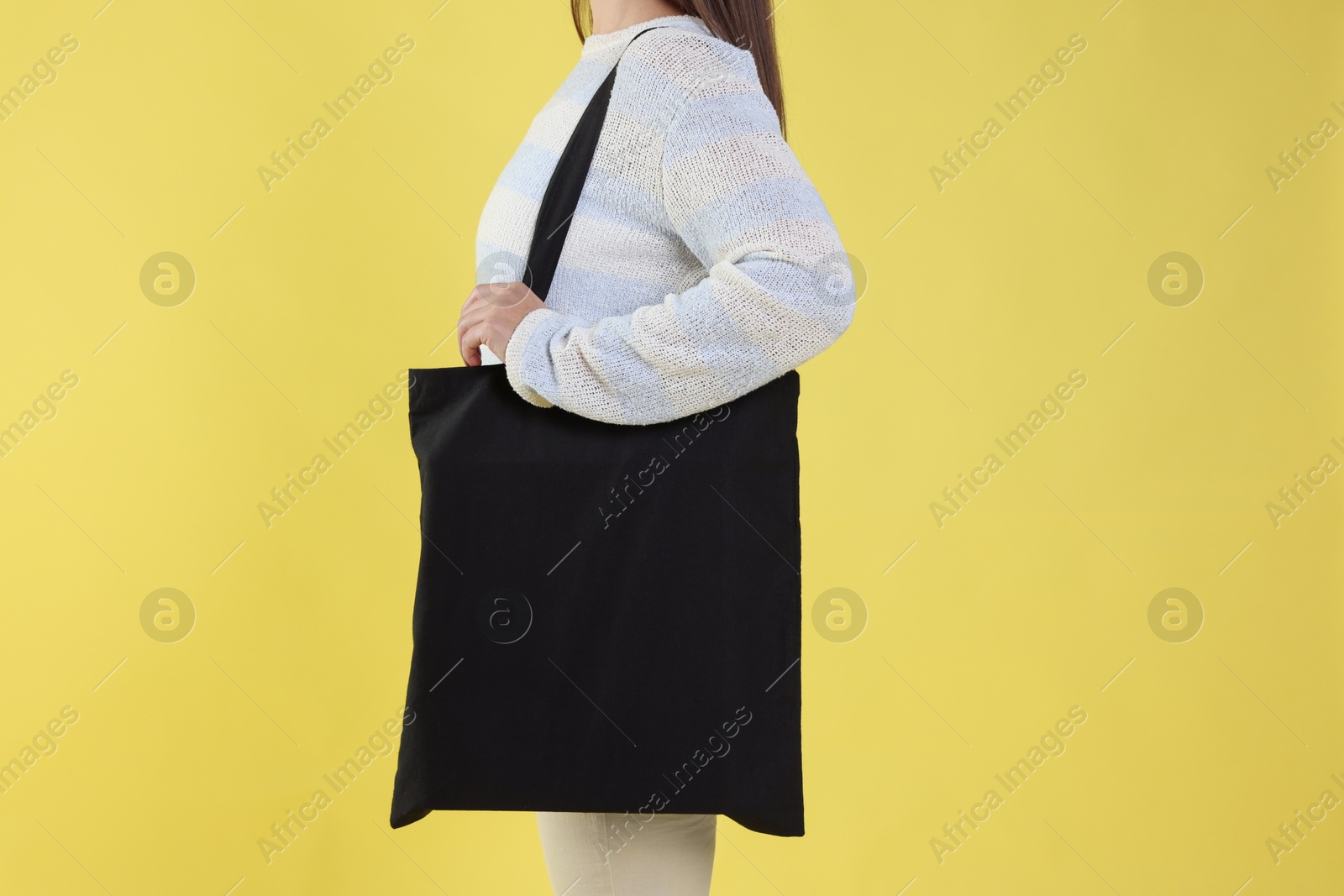 Photo of Woman with blank black shopper bag on yellow background, closeup. Mockup for design