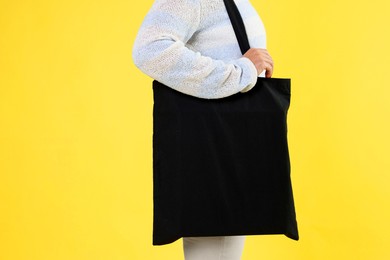 Woman with blank black shopper bag on yellow background, closeup. Mockup for design