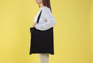 Photo of Woman with blank black shopper bag on yellow background, closeup. Mockup for design