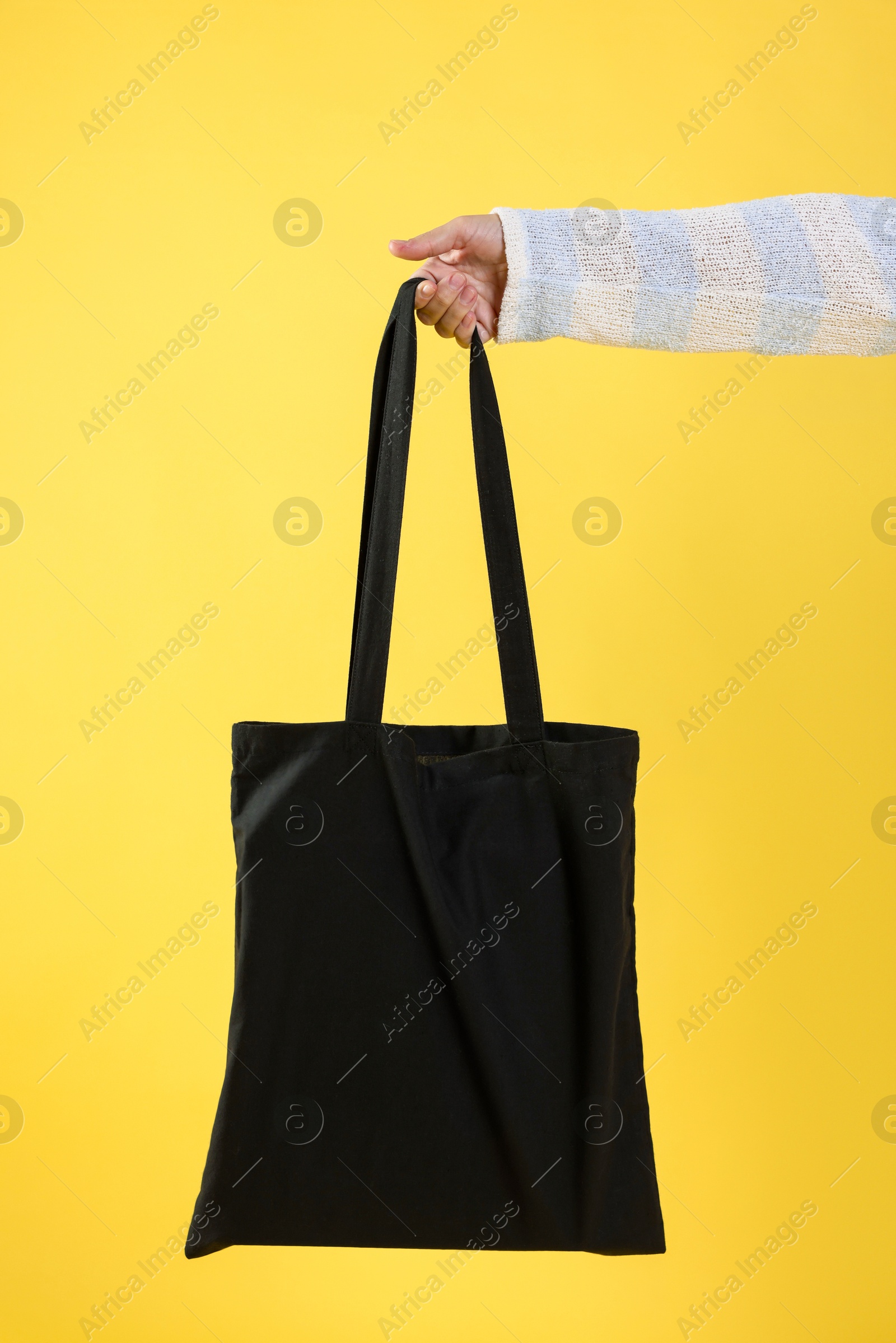 Photo of Woman with blank black shopper bag on yellow background, closeup. Mockup for design