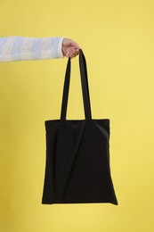 Photo of Woman with blank black shopper bag on yellow background, closeup. Mockup for design