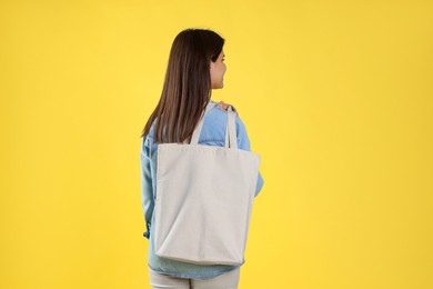 Photo of Woman with blank shopper bag on yellow background, back view. Mockup for design