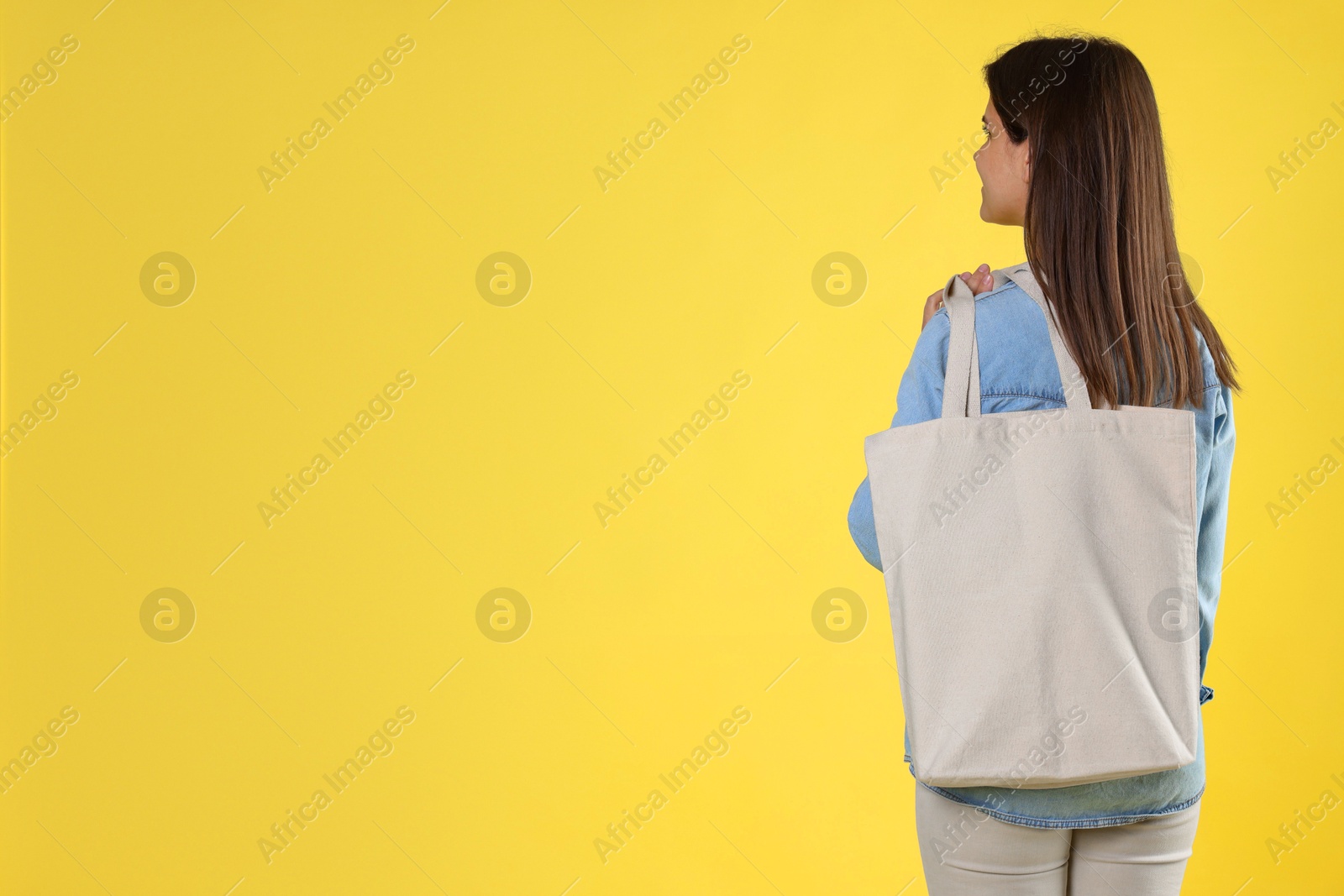 Photo of Woman with blank shopper bag on yellow background, back view. Mockup for design