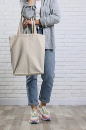 Woman with blank shopper bag near white brick wall, closeup. Mockup for design