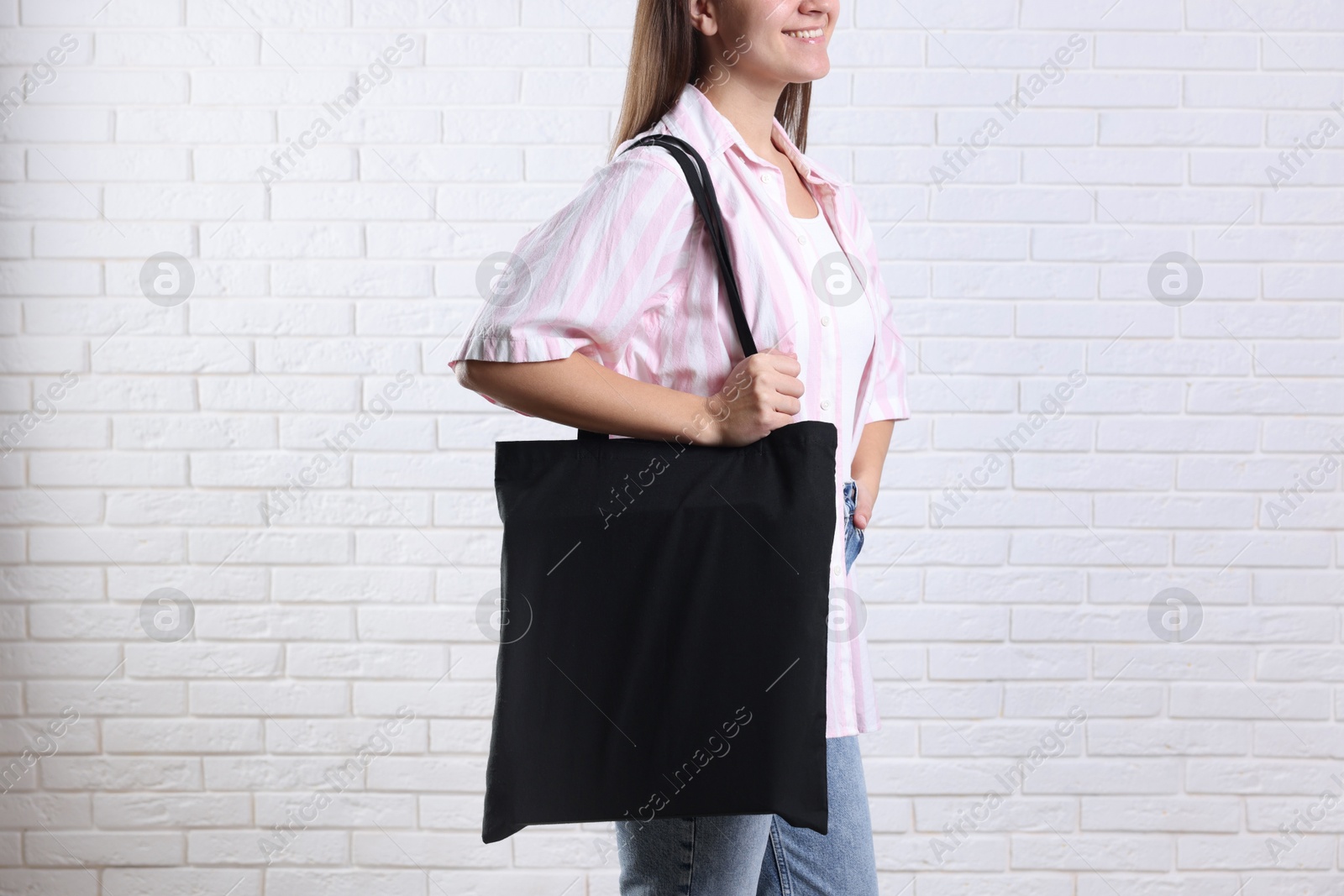 Photo of Woman with blank black shopper bag near white brick wall, closeup. Mockup for design