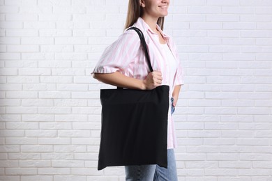 Photo of Woman with blank black shopper bag near white brick wall, closeup. Mockup for design