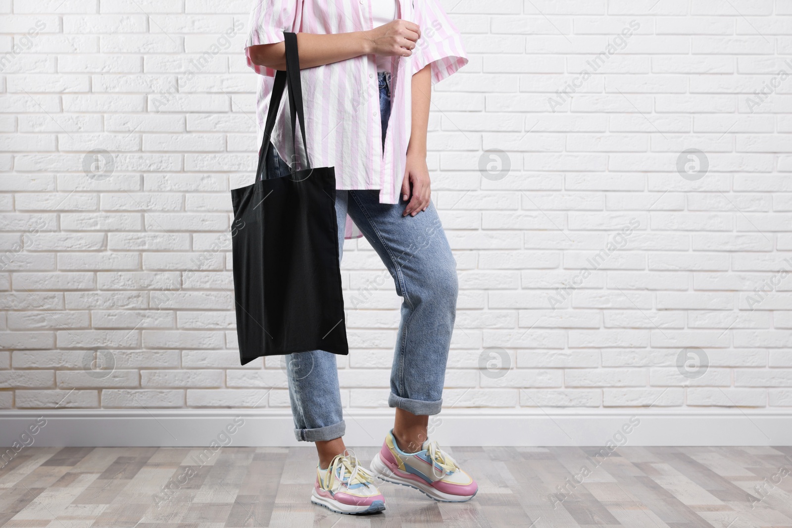 Photo of Woman with blank black shopper bag near white brick wall, closeup. Mockup for design