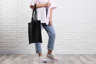 Woman with blank black shopper bag near white brick wall, closeup. Mockup for design