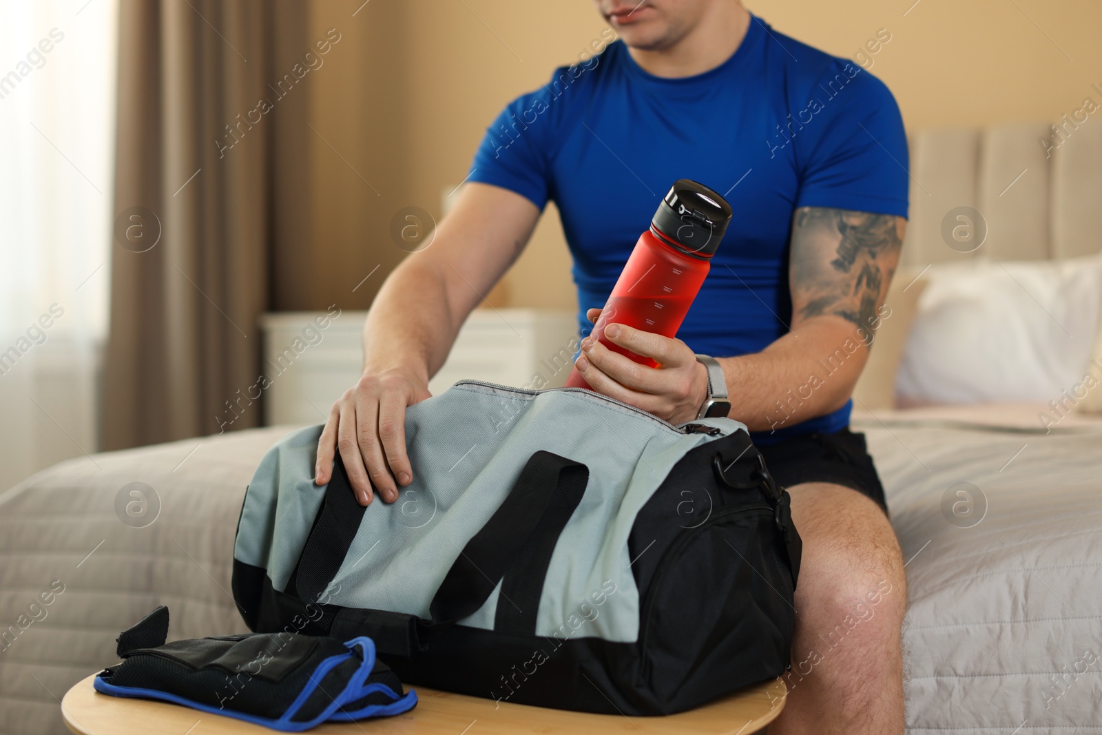 Photo of Man putting bottle of water into gym bag indoors, closeup