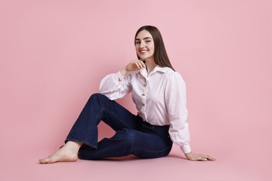 Smiling woman in stylish jeans on pink background