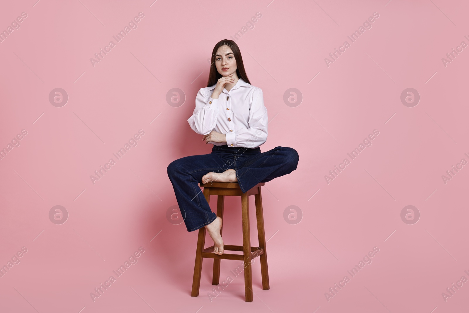 Photo of Beautiful young woman in stylish jeans sitting on stool against pink background