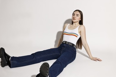 Photo of Beautiful young woman in stylish jeans posing on light background