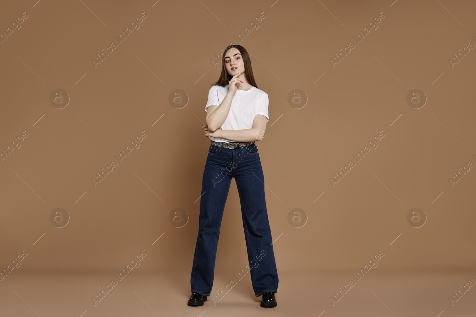 Photo of Beautiful young woman in stylish jeans on brown background