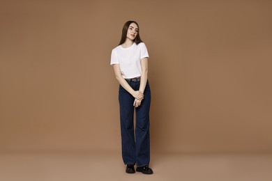 Photo of Beautiful young woman in stylish jeans on brown background