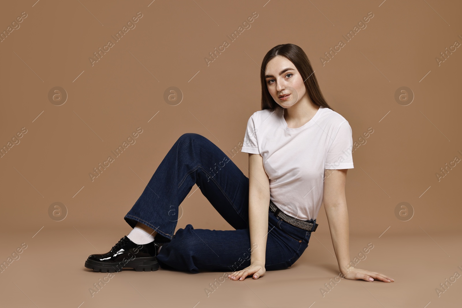 Photo of Beautiful young woman in stylish jeans on brown background