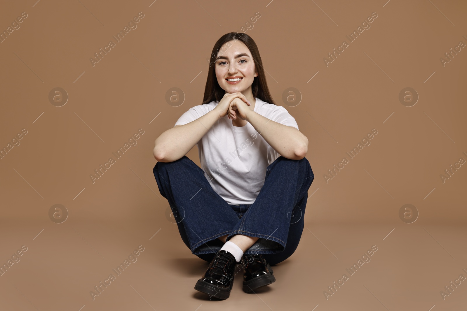 Photo of Smiling woman in stylish jeans on brown background