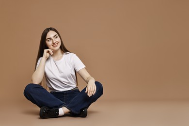 Photo of Smiling woman in stylish jeans on brown background. Space for text