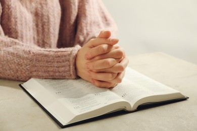 Photo of Woman with open Holy Bible praying at beige table, closeup