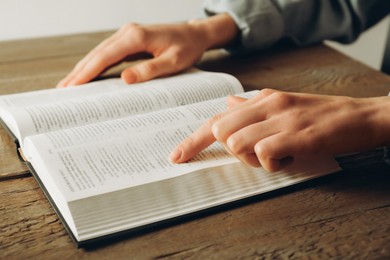 Photo of Woman reading Holy Bible in English language at wooden table, closeup