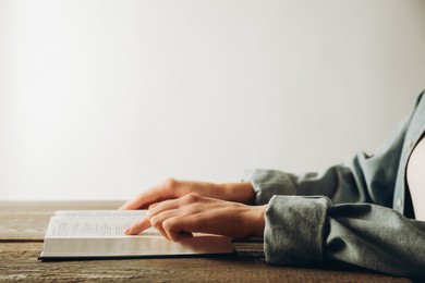 Photo of Woman reading Holy Bible in English language at wooden table, closeup