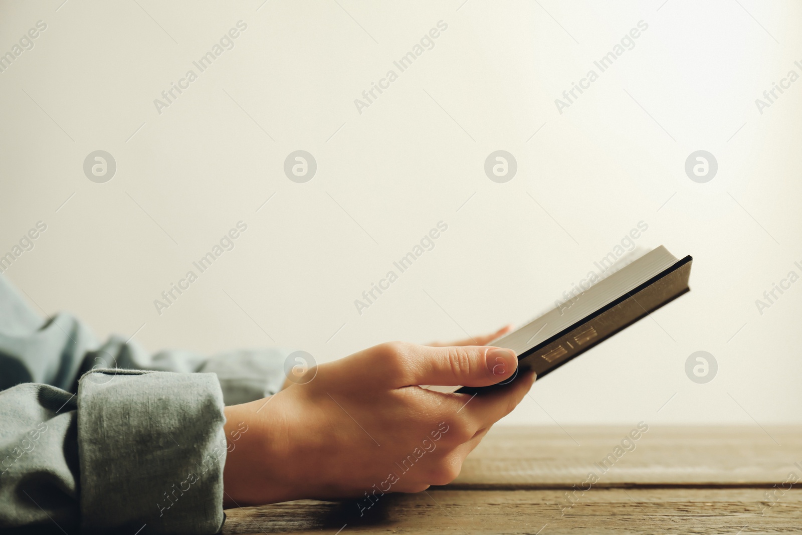 Photo of Woman reading Holy Bible at wooden table, closeup