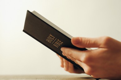 Woman with Holy Bible against beige background, closeup