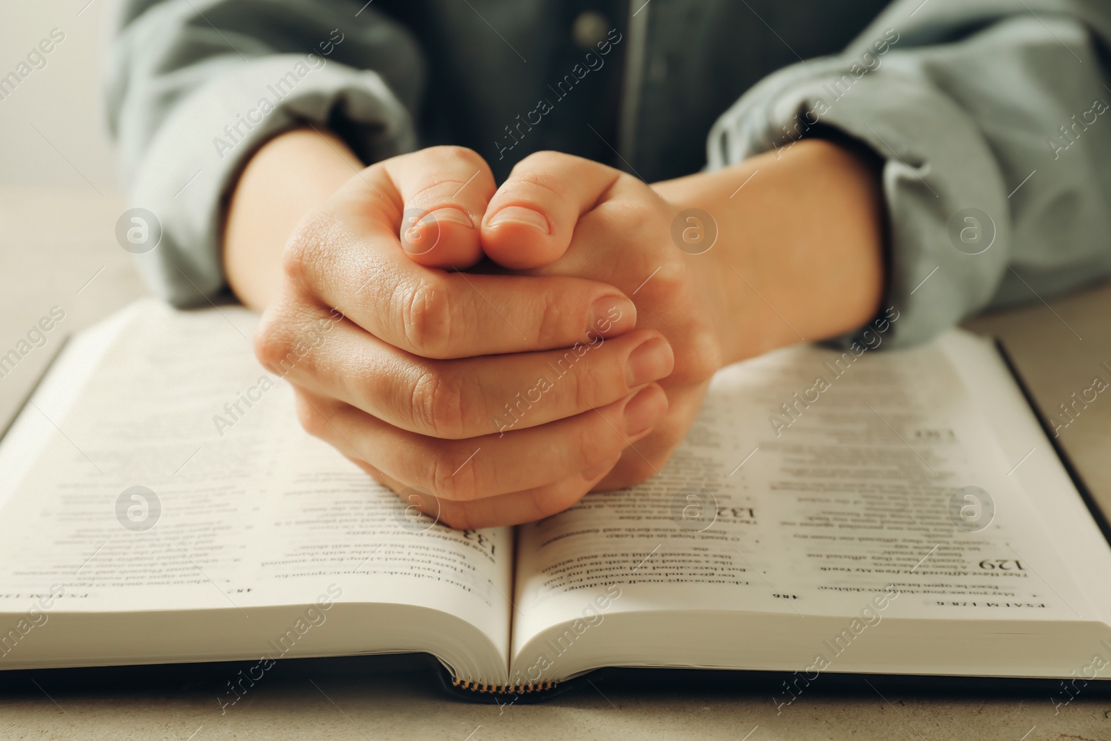 Photo of Woman with open Holy Bible in English language praying at beige table, closeup