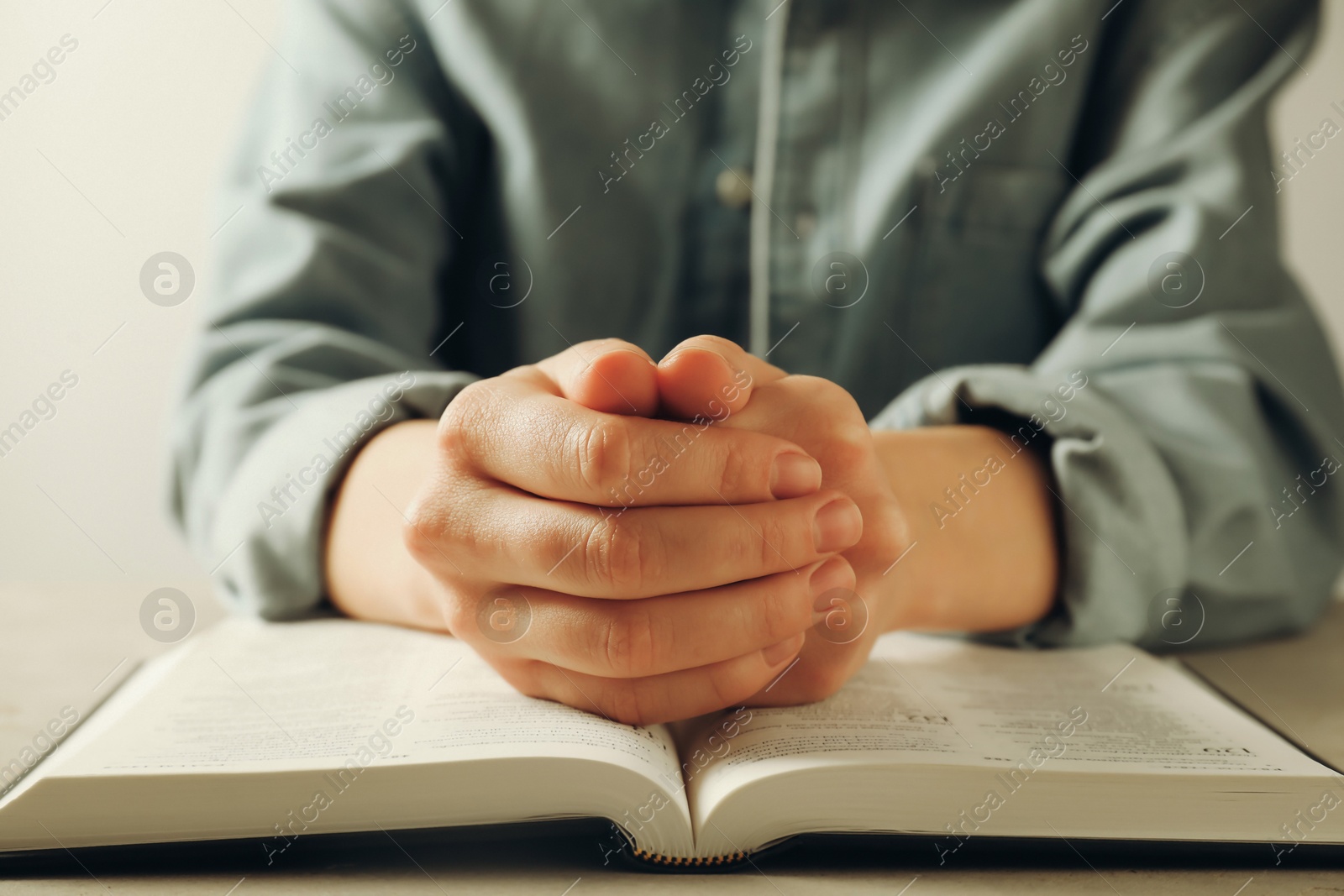 Photo of Woman with open Holy Bible in English language praying at beige table, closeup