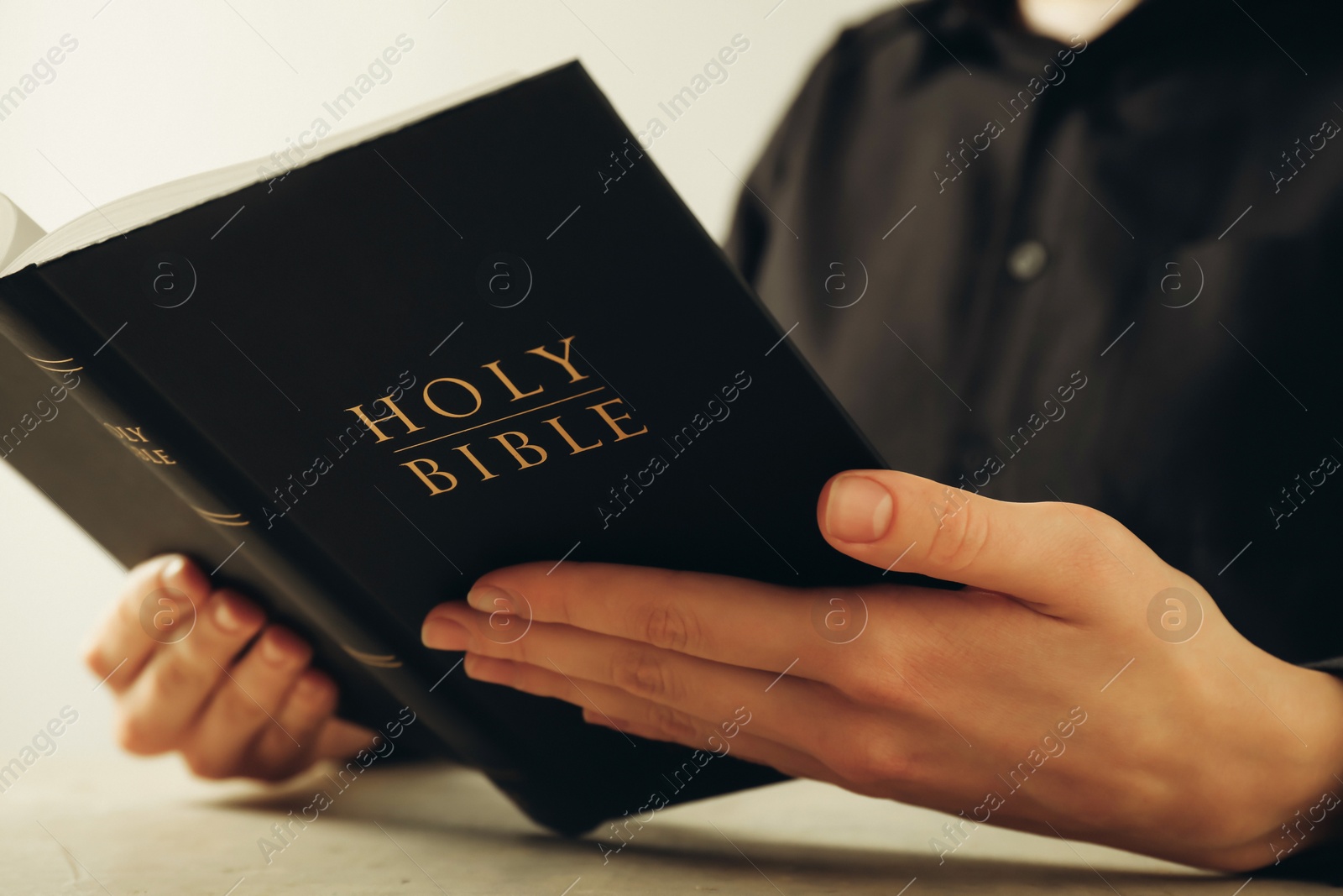 Photo of Woman reading Holy Bible at beige table, closeup