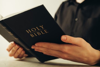 Woman reading Holy Bible at beige table, closeup