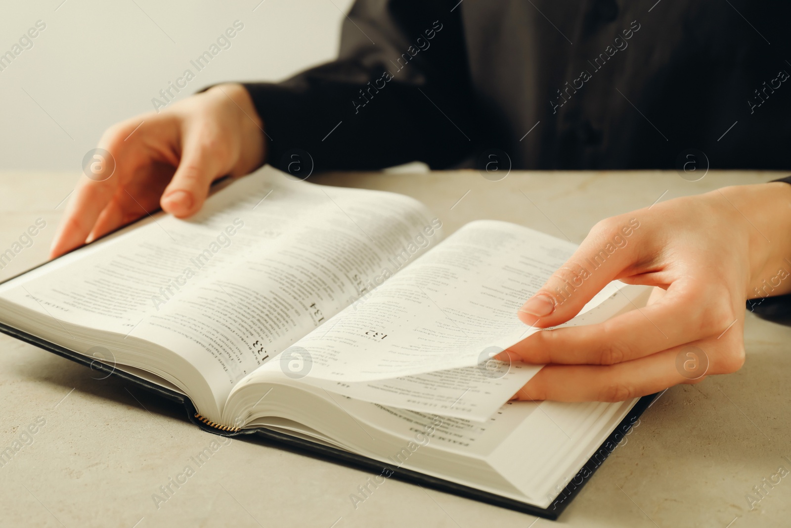 Photo of Woman reading Holy Bible in English language at beige table, closeup