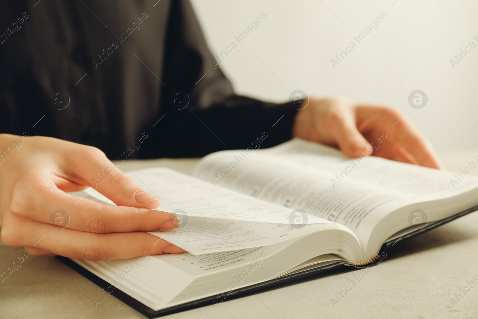 Photo of Woman reading Holy Bible at beige table, closeup