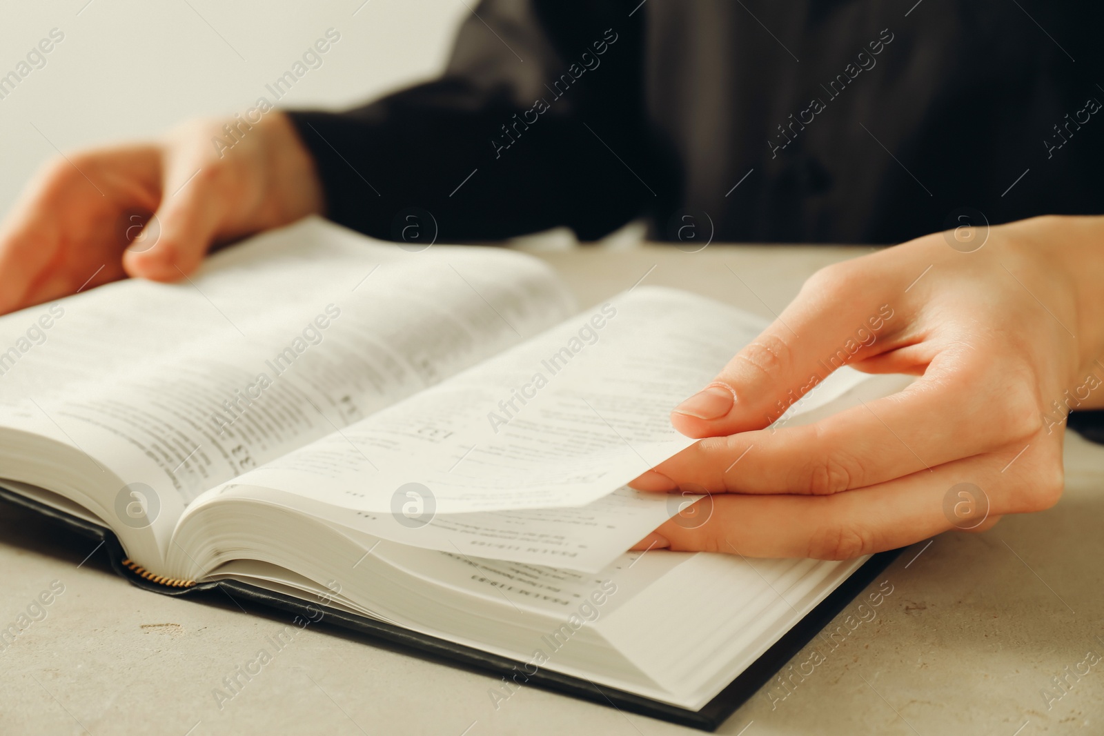 Photo of Woman reading Holy Bible in English language at beige table, closeup