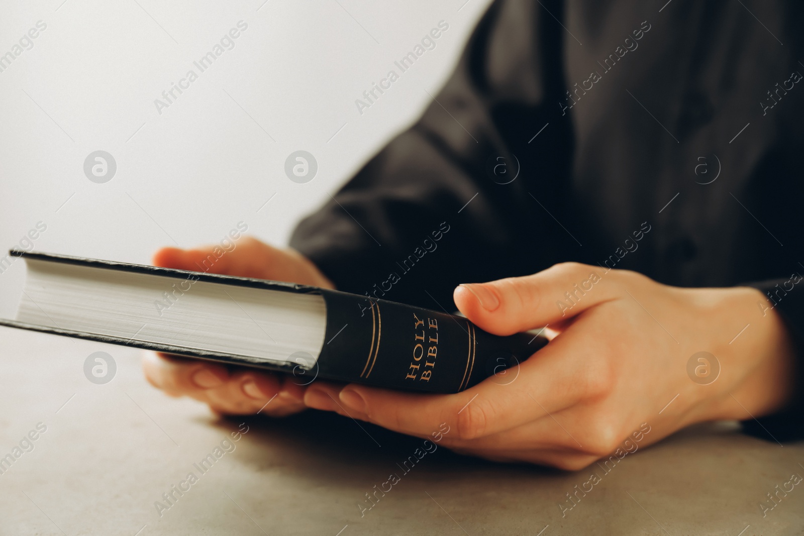 Photo of Woman with hardcover Holy Bible at beige table, closeup