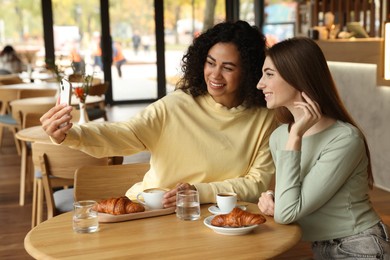 Happy friends taking selfie during coffee meeting in cafe