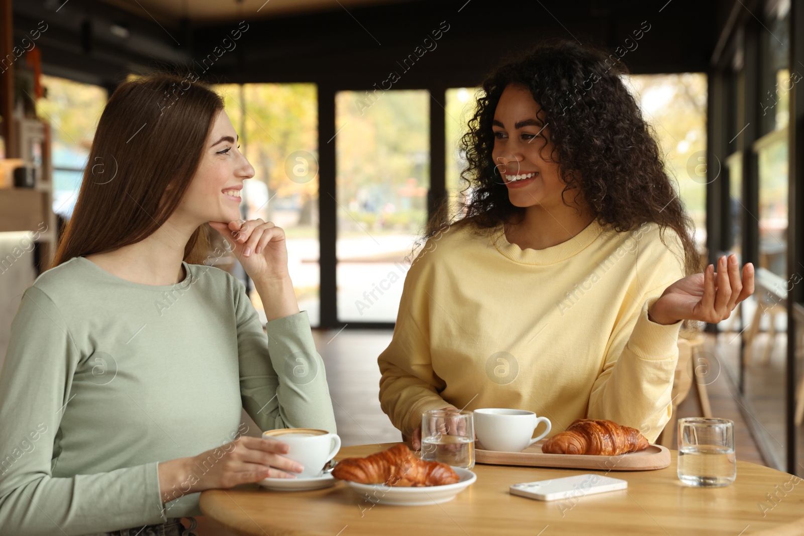 Photo of Happy women with coffee drinks chatting in cafe