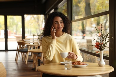 Woman with cup of coffee talking on phone in cafe