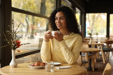 Photo of Woman with coffee and croissant at table in cafe