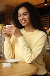 Woman with cup of coffee at table in cafe