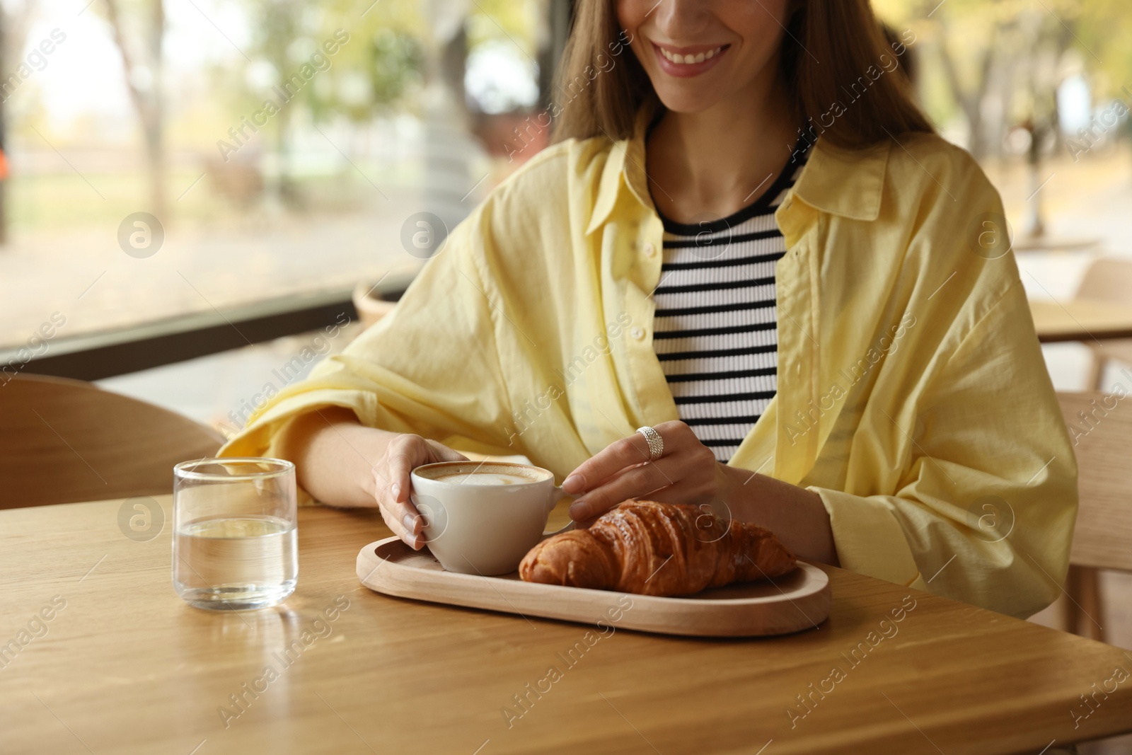 Photo of Woman with coffee and croissant at table in cafe, closeup