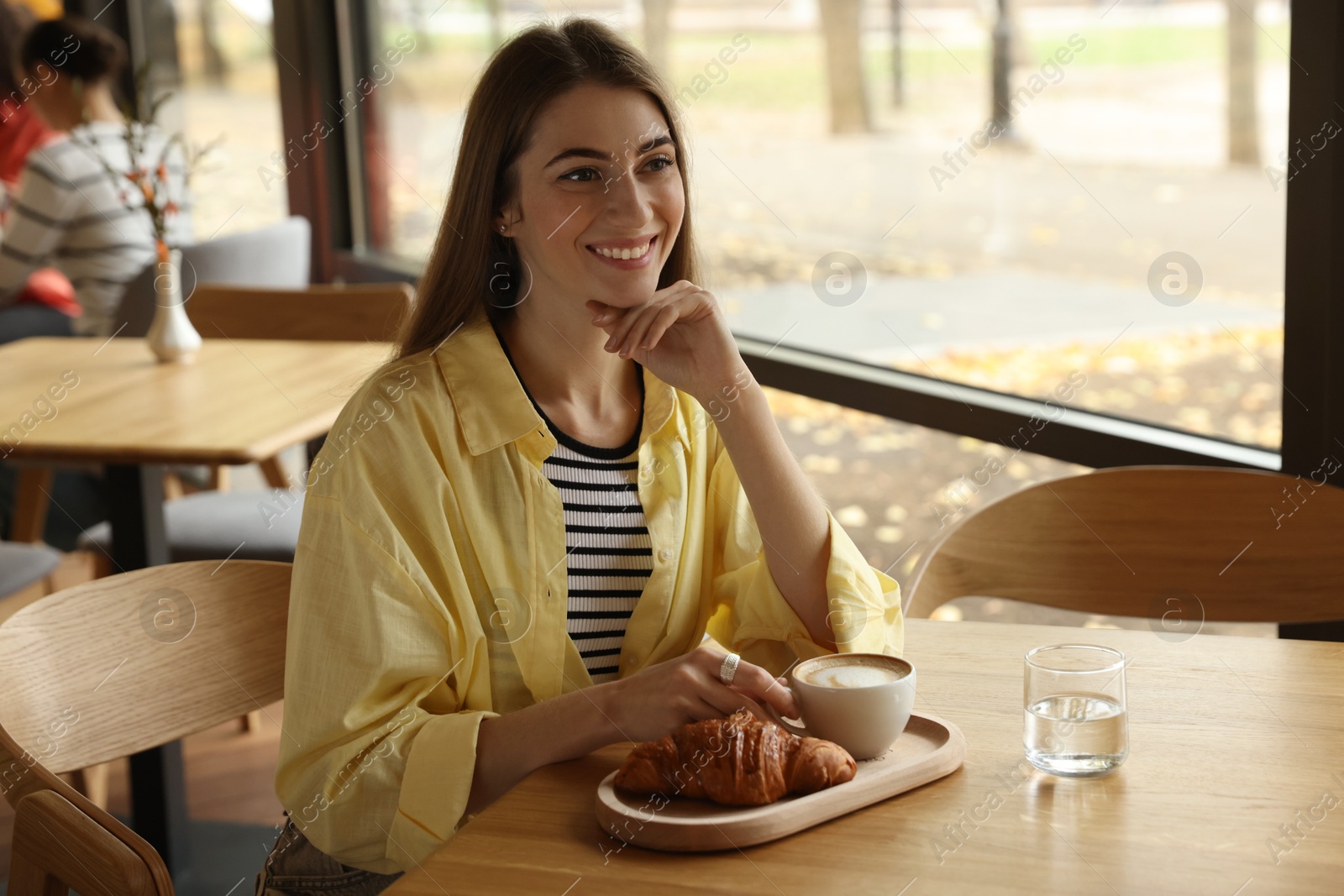 Photo of Woman with coffee and croissant at table in cafe