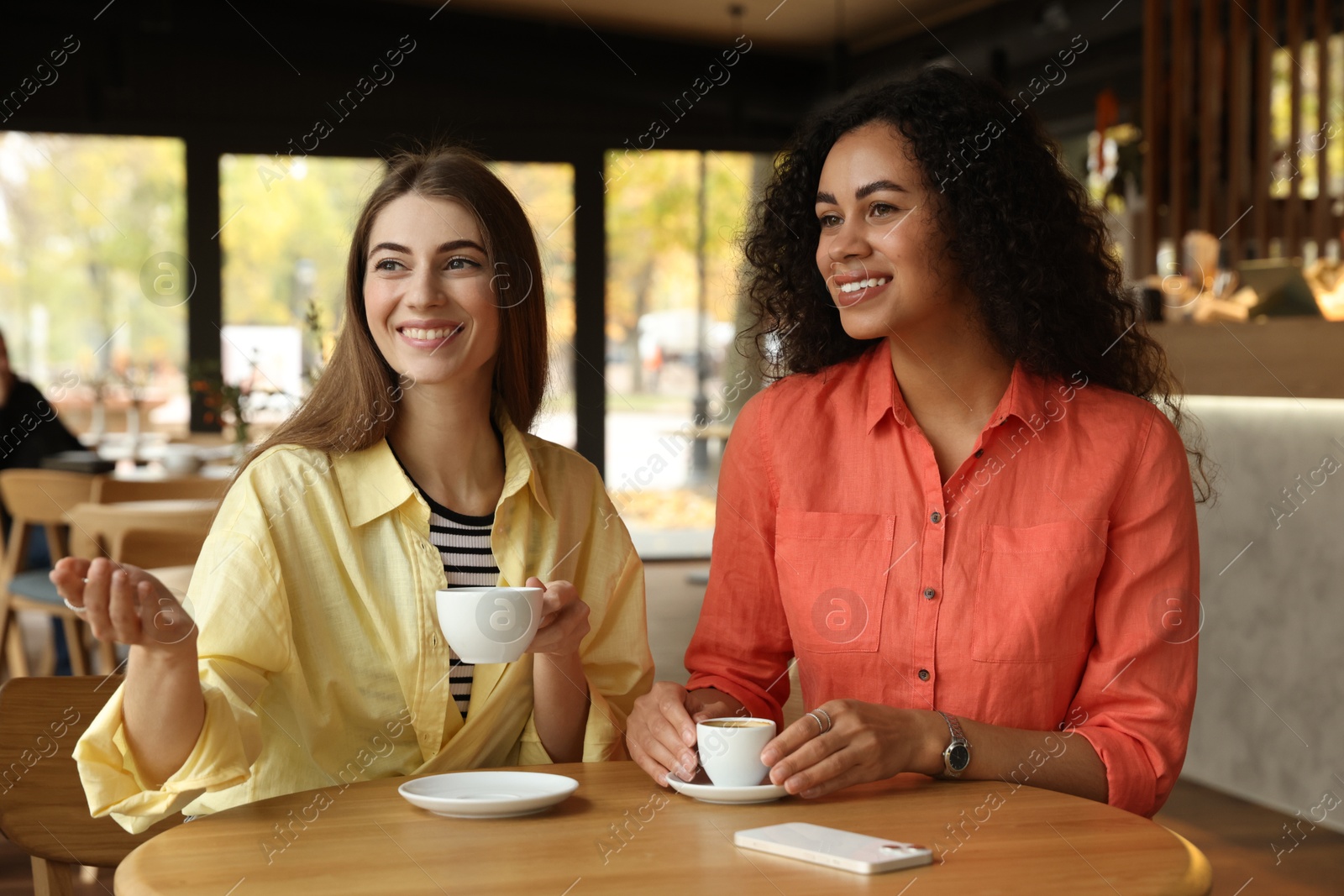 Photo of Happy women with coffee drinks chatting in cafe