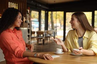 Happy women with coffee drinks chatting in cafe