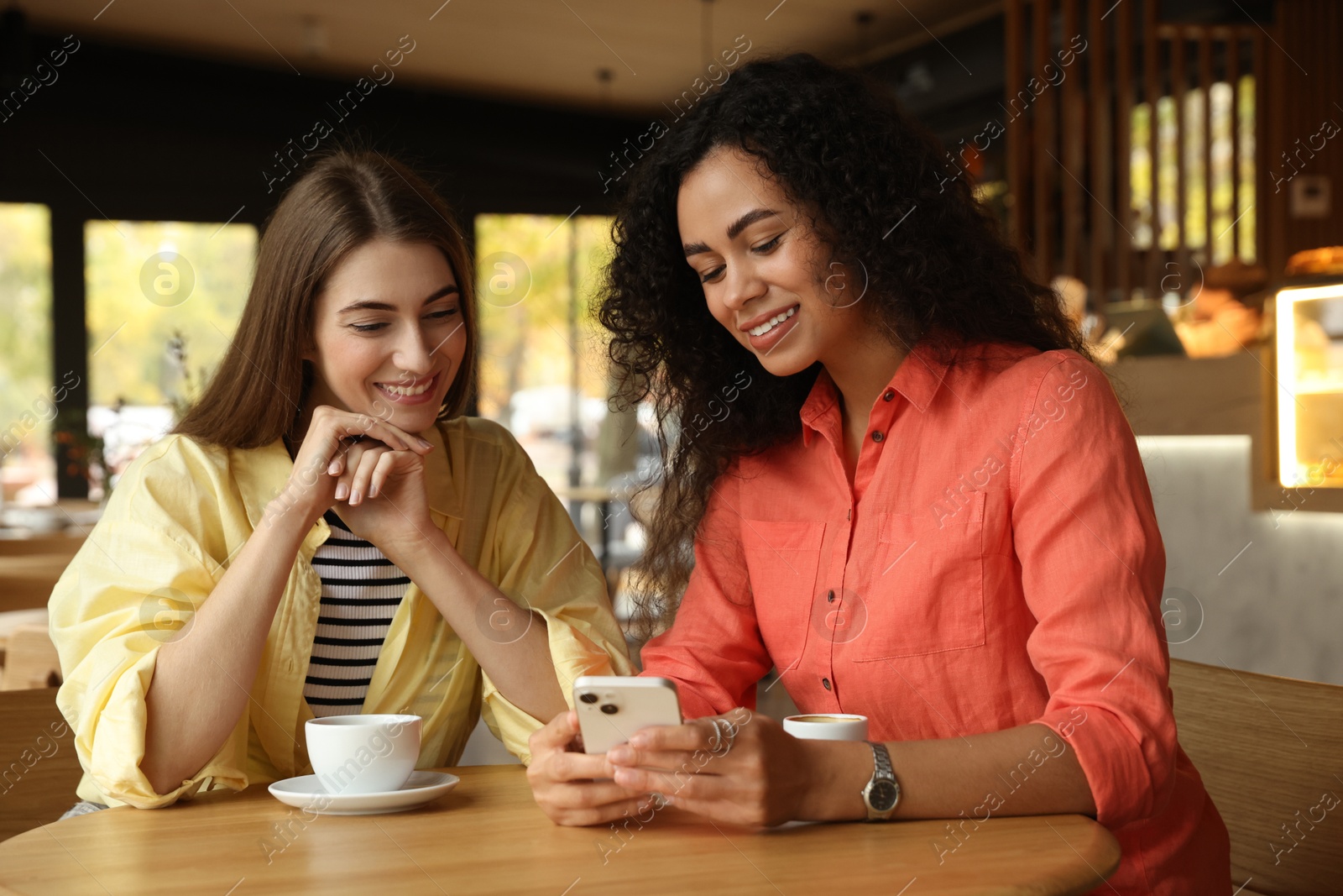 Photo of Women using smartphone while having coffee in cafe