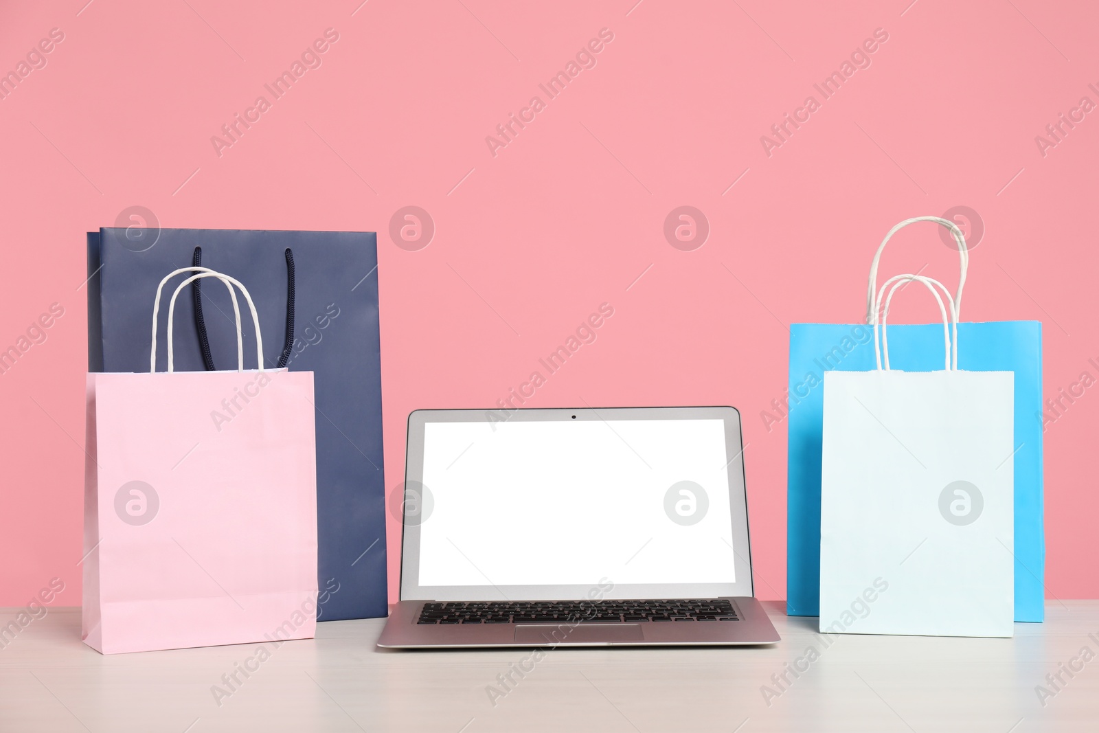 Photo of Internet shopping. Laptop and colorful paper bags on table against pink background