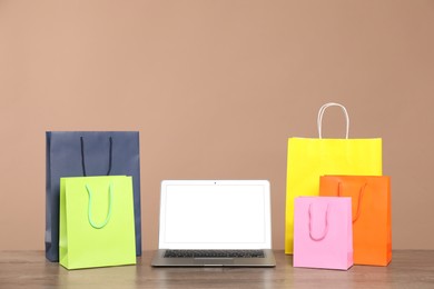 Photo of Internet shopping. Laptop and colorful paper bags on wooden table against brown background