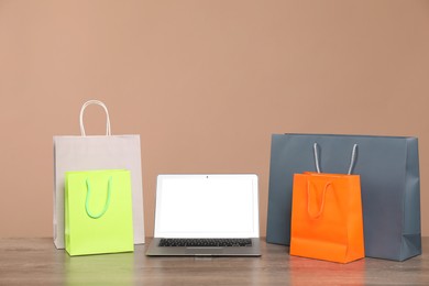 Photo of Internet shopping. Laptop and colorful paper bags on wooden table against brown background