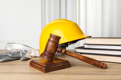 Photo of Accident at work. Gavel, safety equipment and stack of books on wooden table, closeup